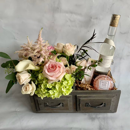 Floral arrangement in a wooden box with a bottle of wine on a marble surface